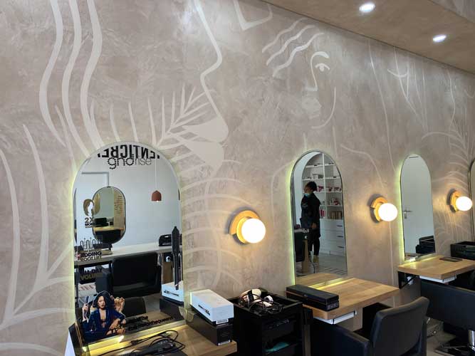 Modern hair salon interior with decorative wall art, arched mirrors, and stylish workstations
