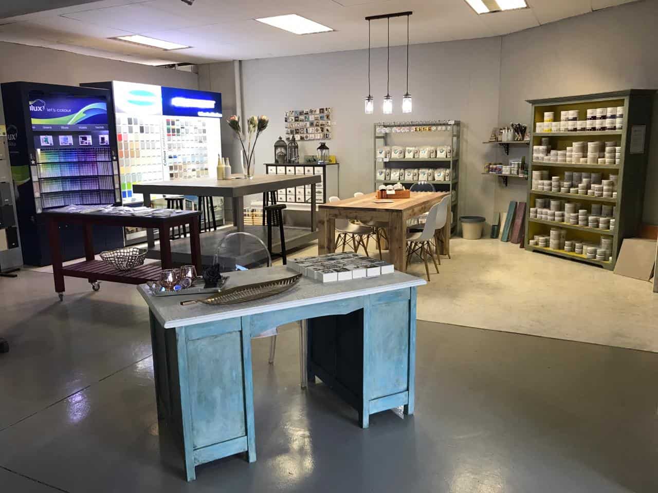 Paint store showroom with color swatches, wooden tables, and shelves stocked with paint cans.