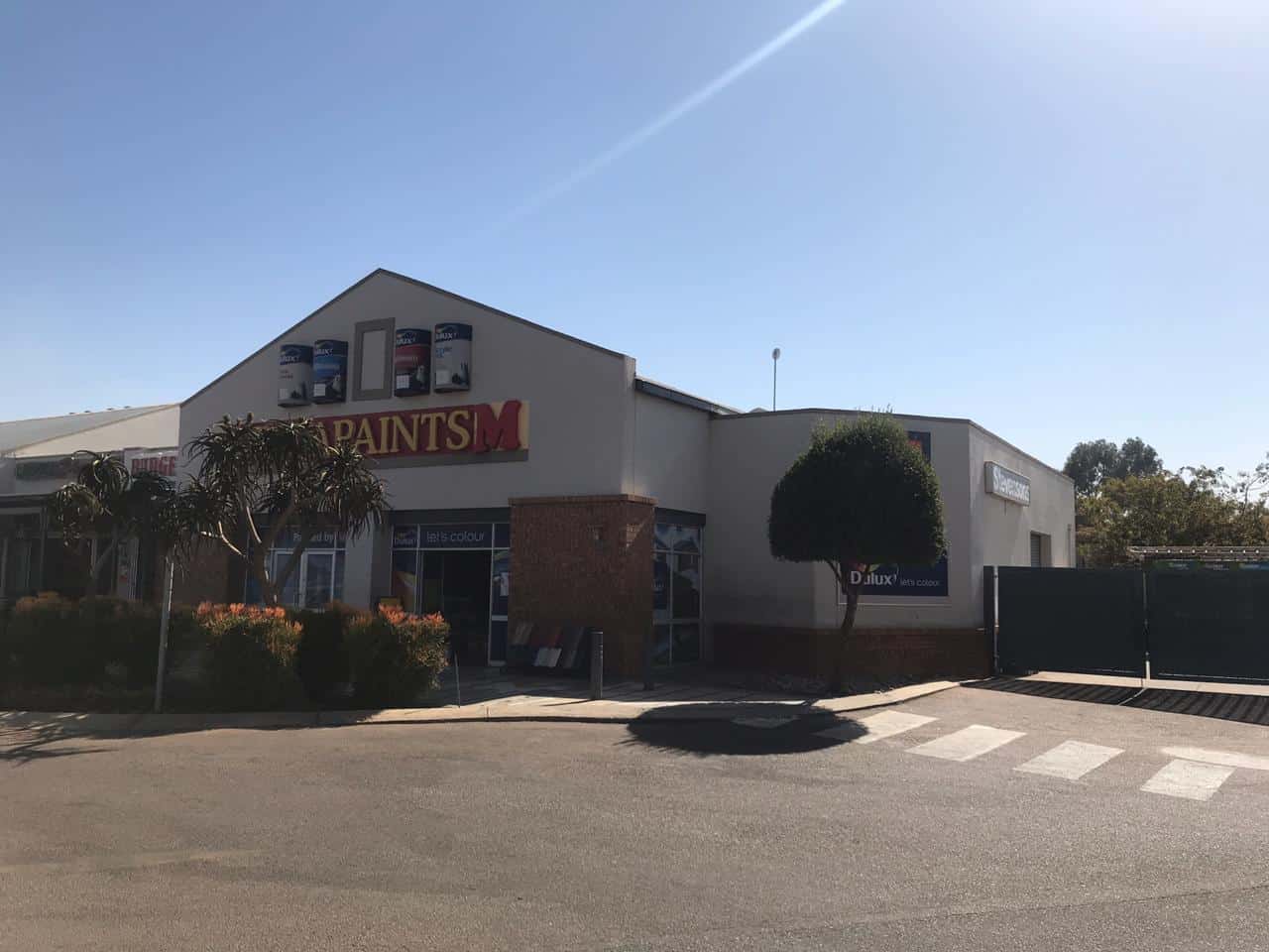 Exterior of a paint store with signage, trees, and clear blue sky.