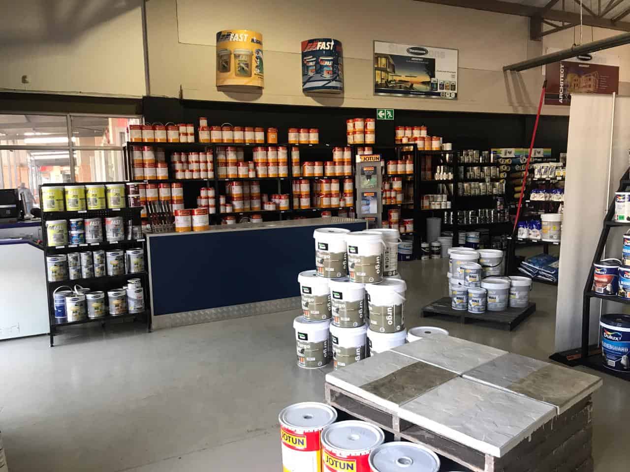 Store interior with shelves full of paint containers and products stacked on pallets.